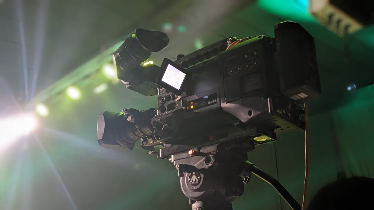Close-up of a professional video camera capturing an event, highlighting its features under stage lighting.