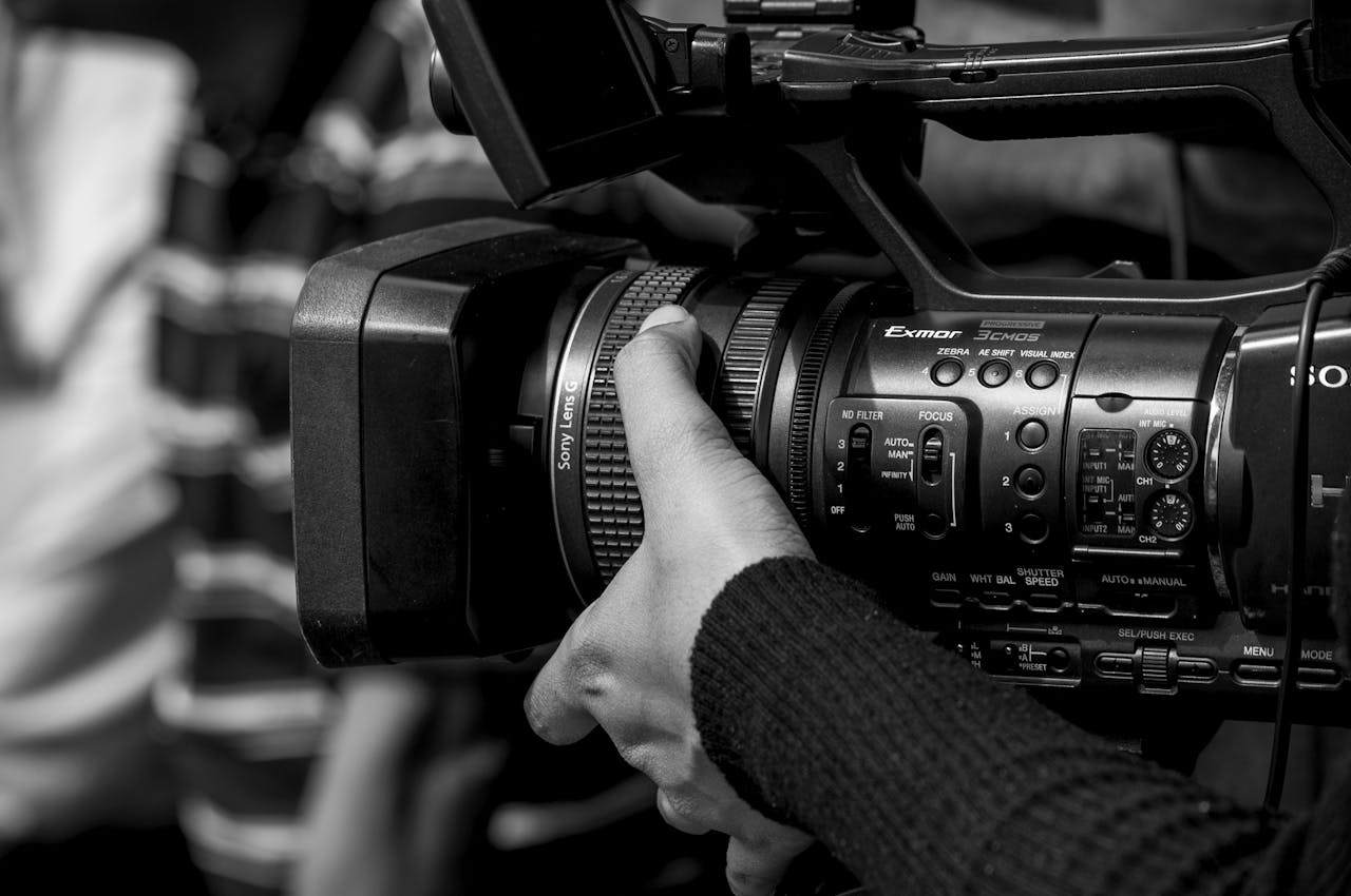 Home Black and white image of a person operating a professional video camera, showcasing detailed camera controls.